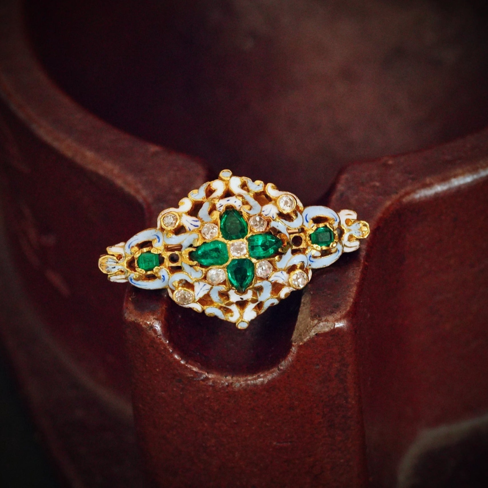 A timeless 1.5 ct Colombian emerald and diamond brooch, available with Jogani, crafted in a Renaissance Revival style with delicate blue and white enamel.