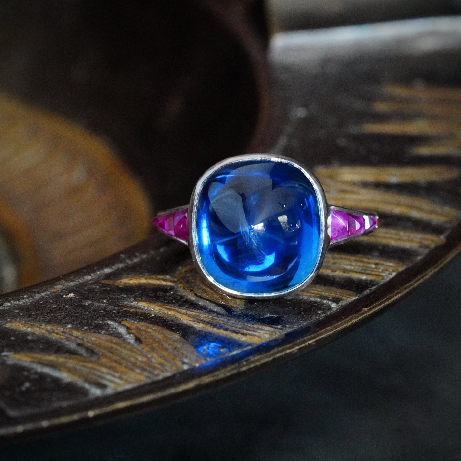 This platinum ring showcases a 10.99 ct no-heat Burma sapphire in a smooth sugarloaf cut, accented by eight rubies. A refined masterpiece from Jogani.