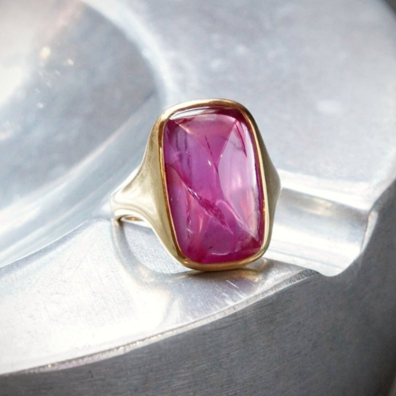 A remarkable 12.00 ct sugarloaf Burma ruby, no heat, glowing with an intense pink hue. Encased in a refined 18K gold bezel setting, this exceptional piece is available at Jogani.