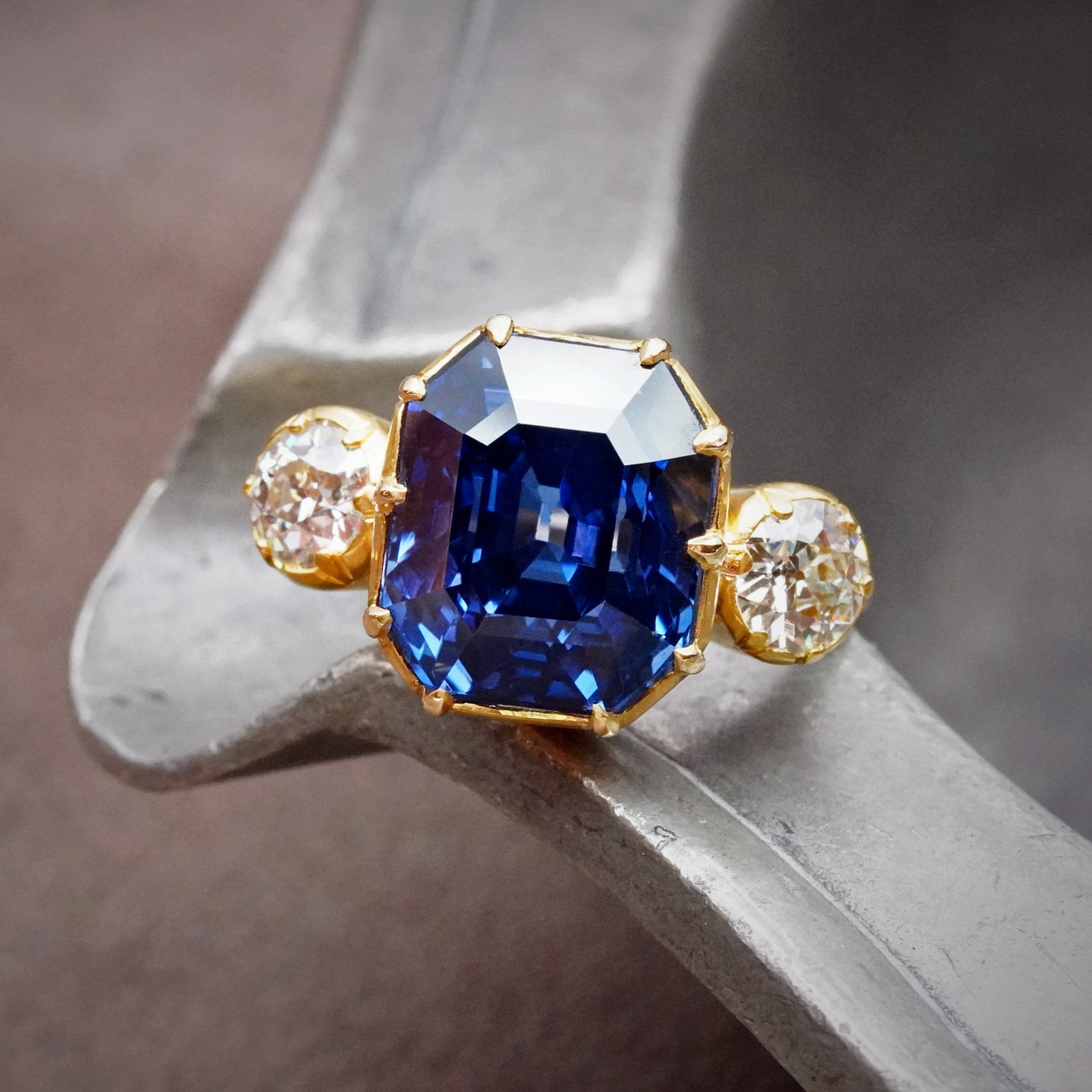 Crafted by Jogani, this 12.81 ct no-heat Madagascar sapphire ring, step-cut to perfection, glows with deep blue intensity. Set in 22K yellow gold with diamond accents.