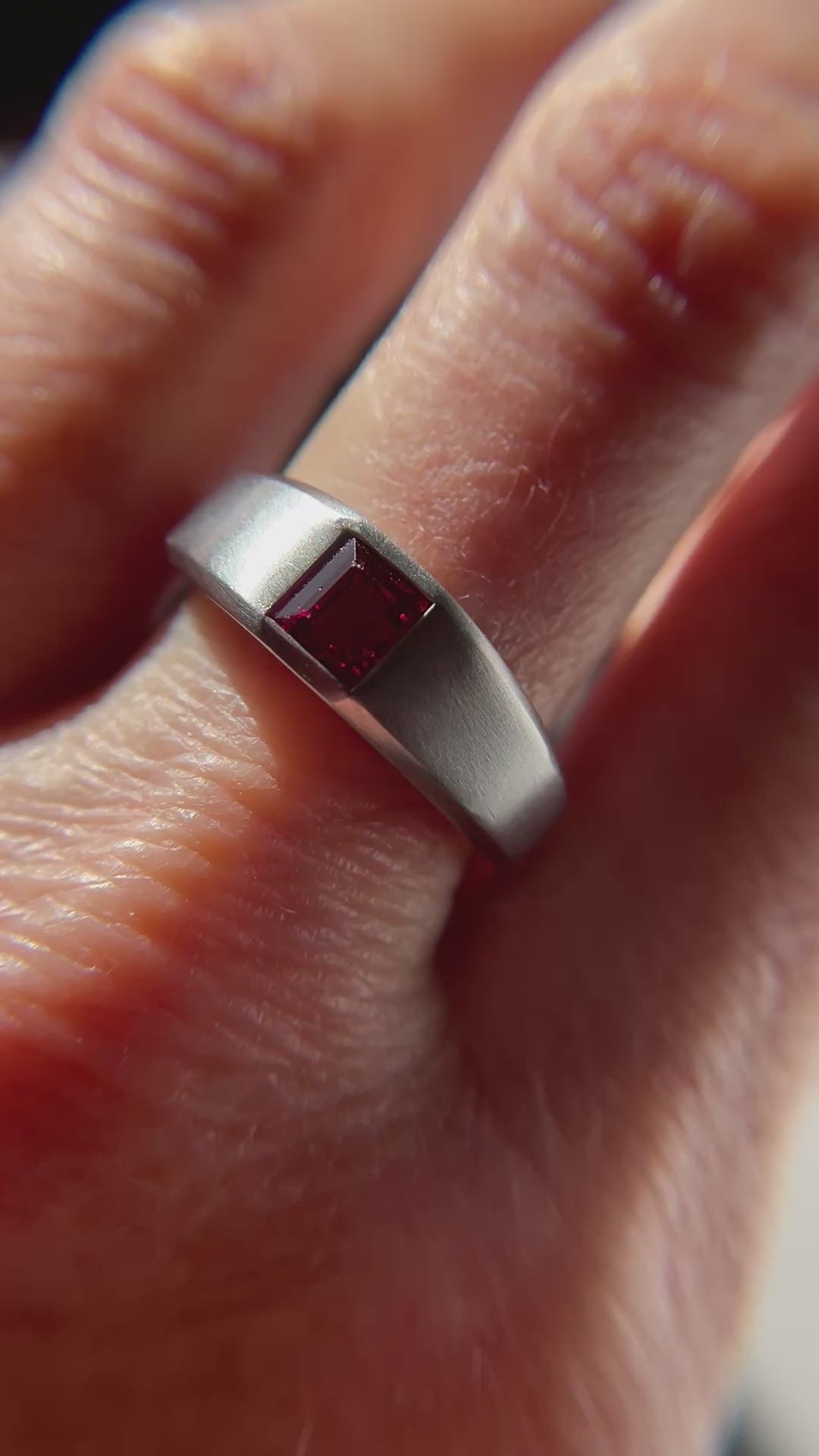 A 1.15-carat step-cut Burmese ruby ring, featuring a clean red gemstone set in a platinum flush setting, worn on a hand, presented by Jogani.