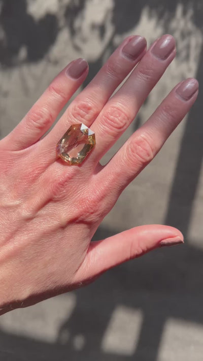 A 13.84-carat step-cut diamond with a fancy brown-yellow color, VVS2 clarity, and type IIa classification, accompanied by a GIA certificate, displayed on a hand under sunlight.