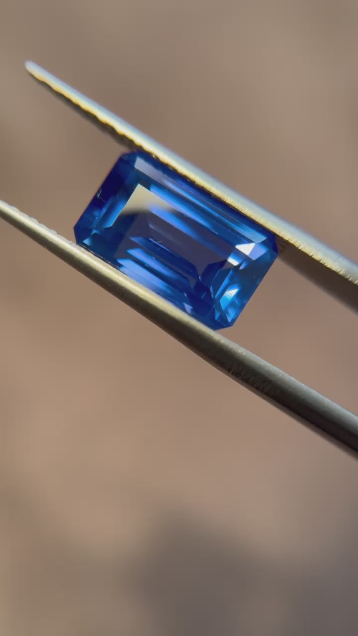 A 6.19-carat step-cut Ceylon sapphire, octagonal in shape, held in tweezers, highlighting its clean clarity and rich blue hue. This unheated sapphire is accompanied by an SSEF certificate, confirming its authenticity and quality. Offered by Jogani, renowned for curating exceptional gemstones.