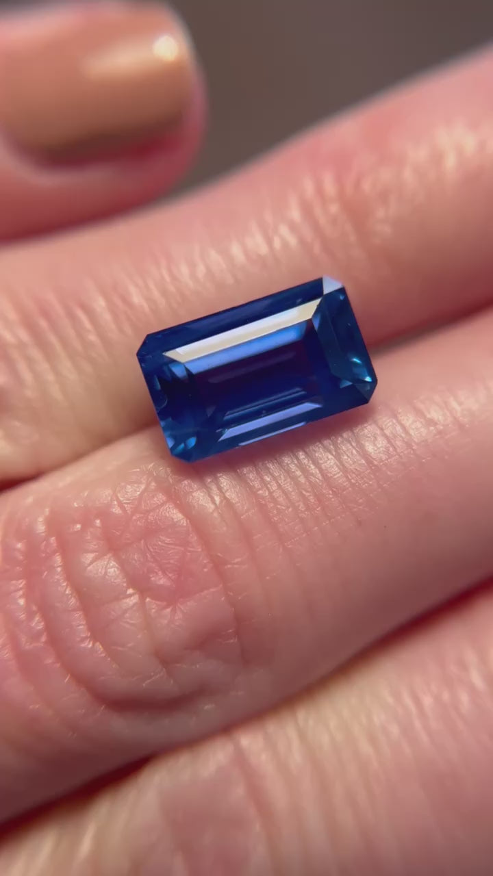 6.19-carat step-cut Ceylon sapphire, octagonal shape, on fingers, showcasing clean clarity and rich blue hue.